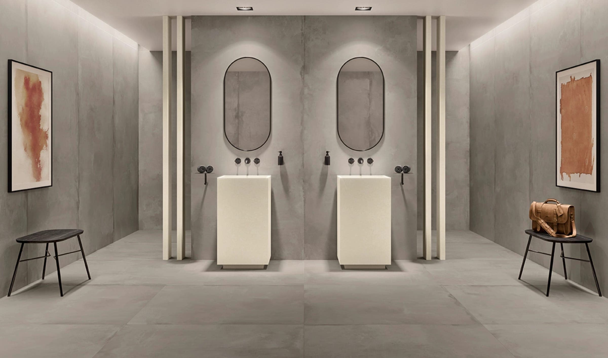 Baño con muros de placas de gran formato, dos lavabos de pedestal y espejos ovalados