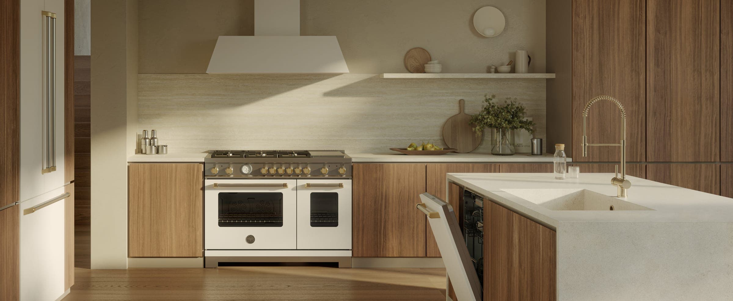 Cocina de muebles de madera y muros beige iluminada por el sol: estufa blanca de dos hornos con perillas doradas bajo una campana de pared blanca; a la izquierda, refrigerador panelado con jaladeras doradas y, a la derecha, lavavajillas entreabierto junto a una isla con tarja y grifo dorado.