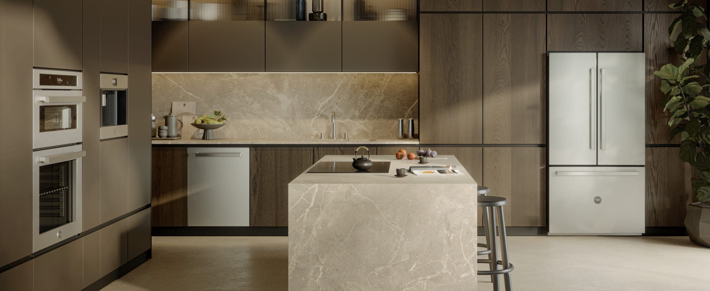 Cocina de muebles de madera oscura y muro de piedra beige: dos hornos de acero empotrados en columna y, al lado, una cafetera empotrada; lavavajillas de acero bajo la barra, refrigerador de acero de dos puertas con cajón congelador a la derecha e isla de piedra con una parrilla de vidrio negro.