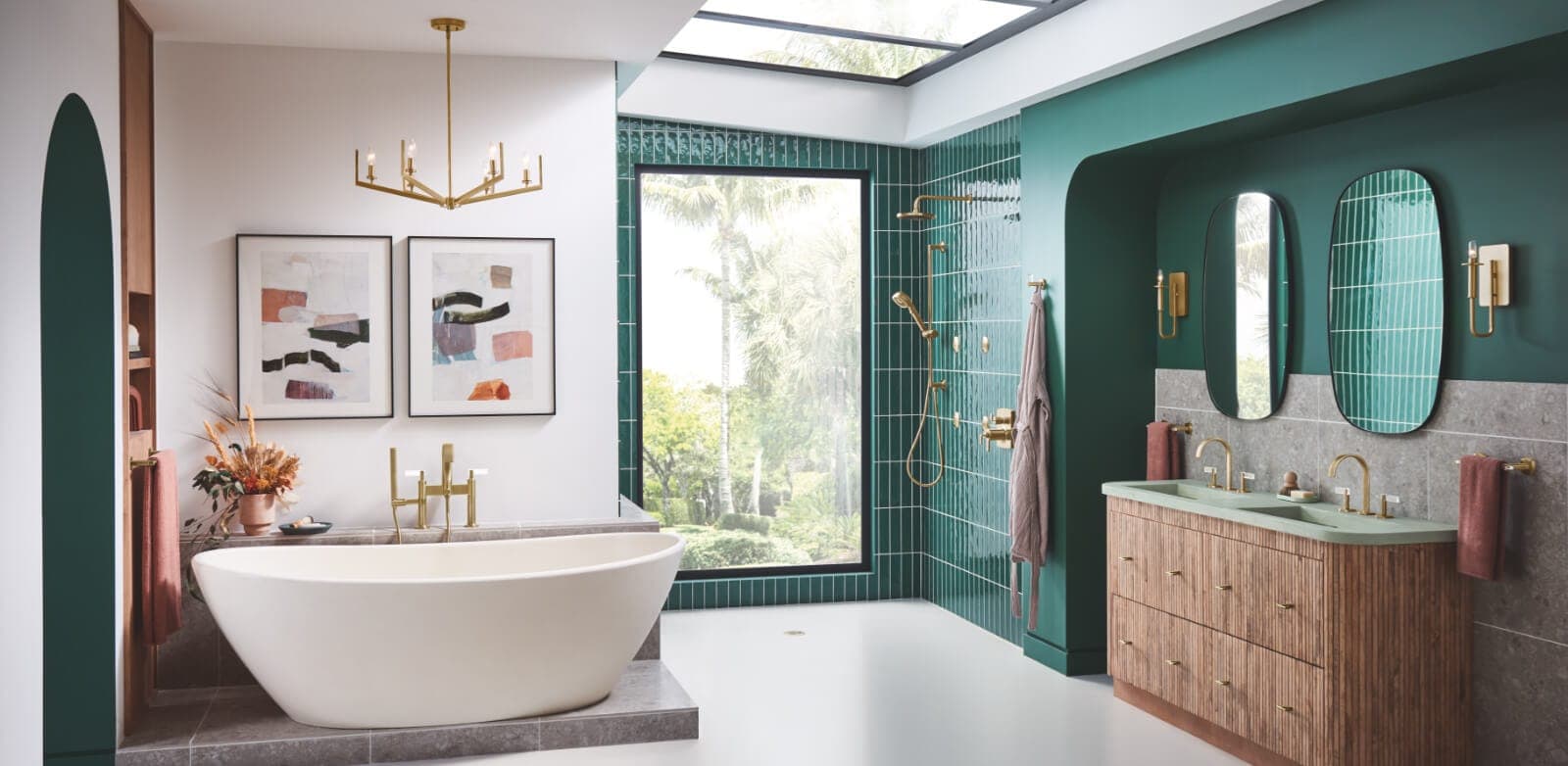 Baño con tina exenta blanca y llave dorada, dos cuadros abstractos y candil dorado; regadera dorada en un muro de azulejo verde junto a una ventana con palmeras y, a la derecha, mueble de madera con dos llaves doradas y dos espejos ovalados.