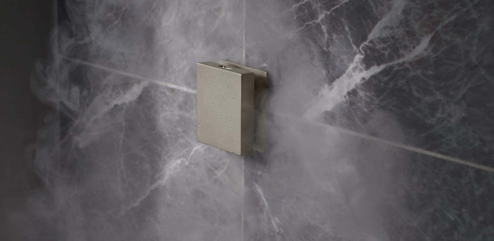 Cabezal de vapor de metal cepillado con gotas de condensación, entre vapor, sobre un muro de mármol gris oscuro