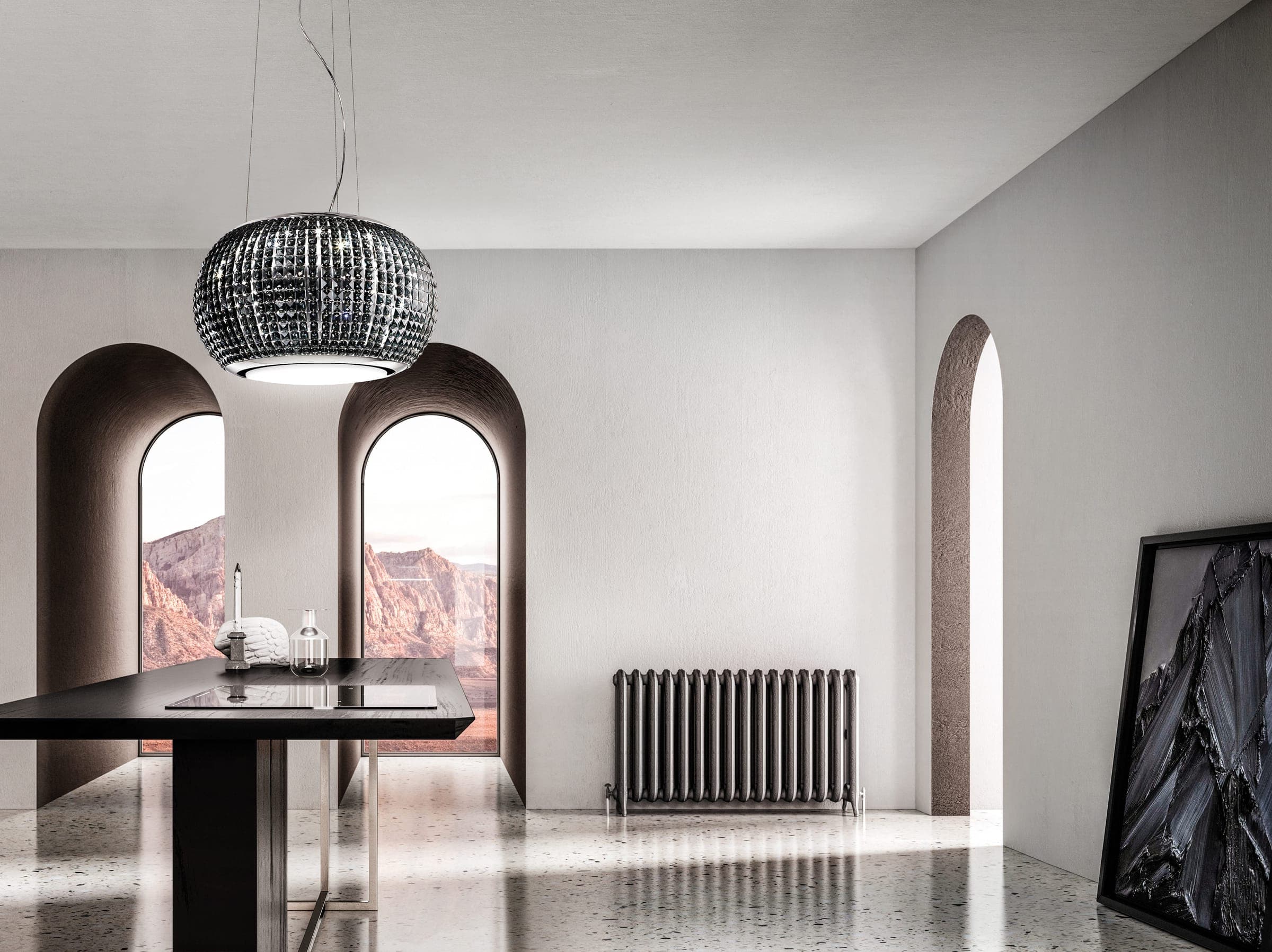Campana suspendida de piezas de cristal oscuro sobre una mesa negra con cubierta de cocción; dos ventanas en arco con un paisaje de rocas rojizas, un radiador metálico, un cuadro oscuro recargado en el muro y piso de terrazo.