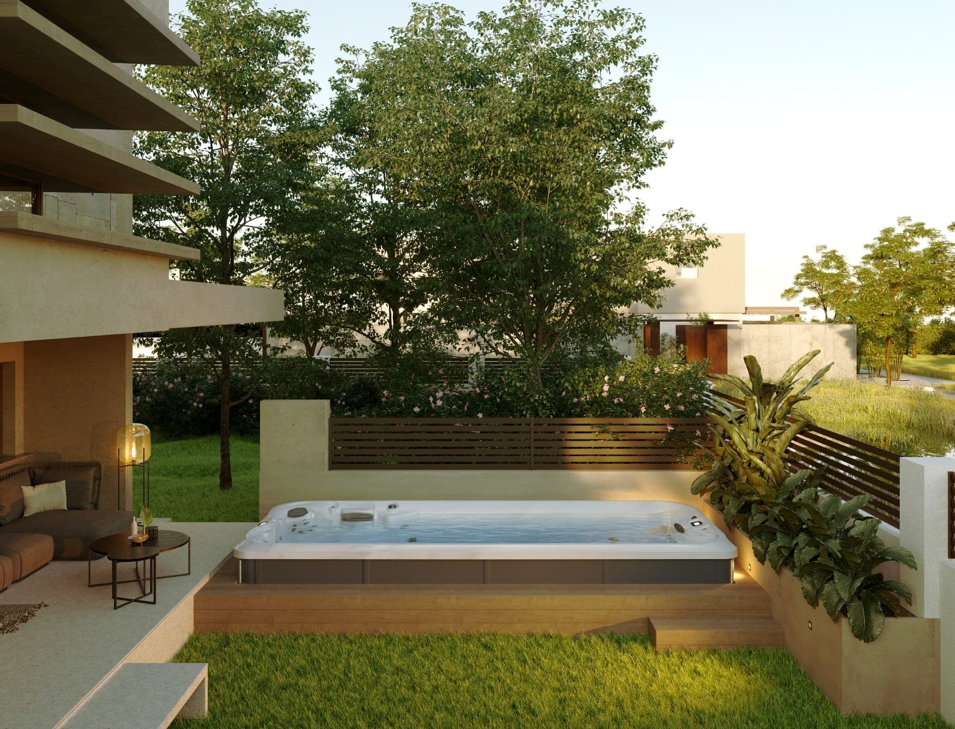 Swim spa de acrílico blanco y gabinete oscuro sobre una plataforma de madera con escalón, en el jardín de una casa contemporánea; jardinera con plantas tropicales, celosía de madera, sala exterior bajo un volado y árboles al fondo.