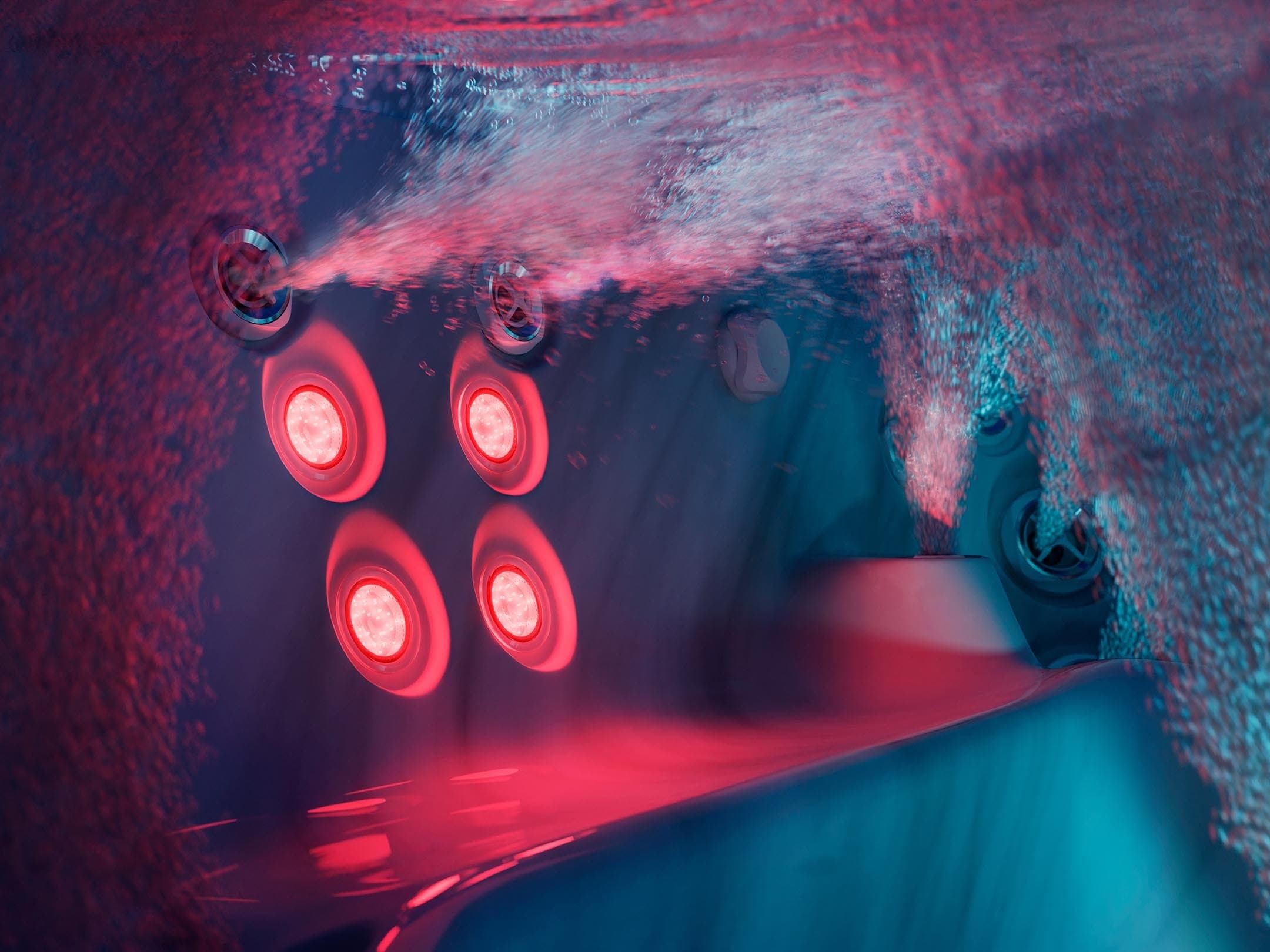 Vista bajo el agua del respaldo de un asiento de spa, con cuatro luces rojas redondas y jets que lanzan chorros de burbujas; reflejos rojos y verde azulados sobre el acrílico.