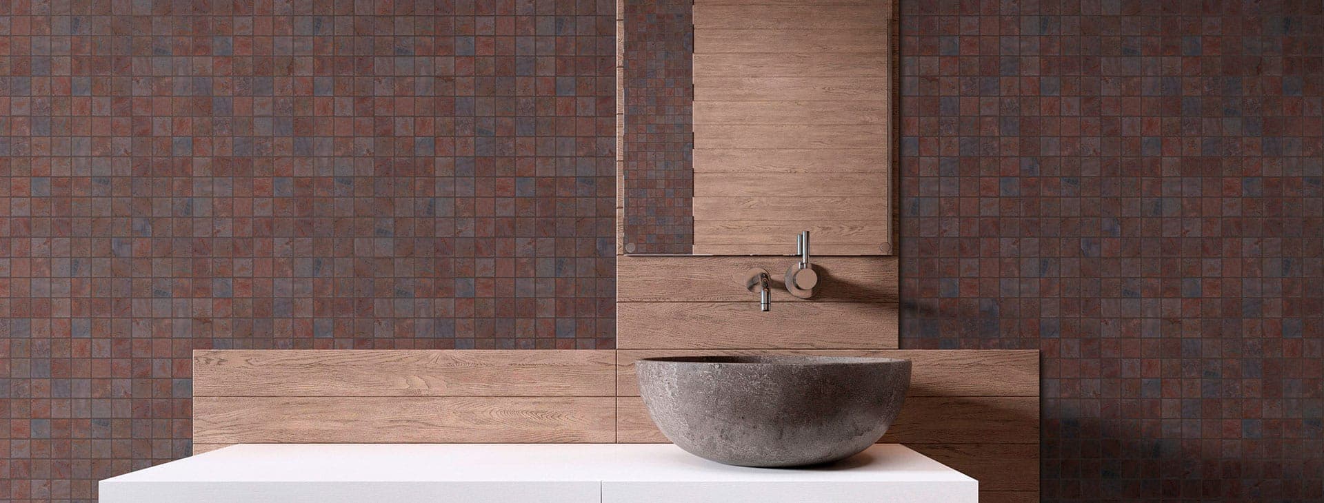 Baño con muros de mosaico cuadrado en tonos rojizos, marrones y grises con textura de piedra, un panel de madera con llave empotrada y un lavabo gris tipo cuenco sobre una cubierta blanca.