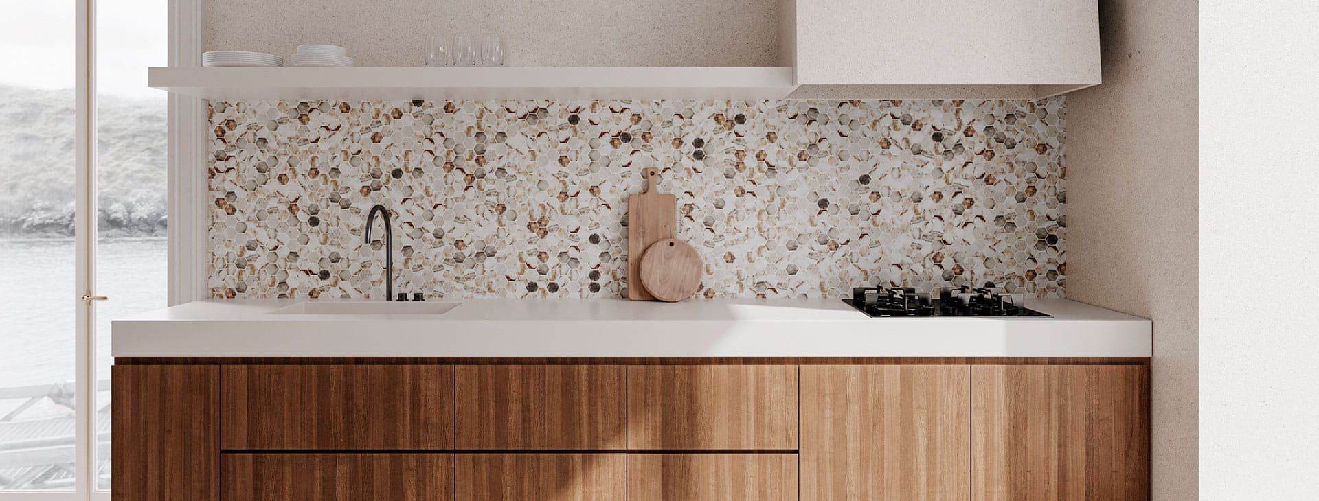 Cocina con muro de mosaico hexagonal en tonos blanco, ámbar y gris con vetas tipo mármol, cubierta blanca con tarja integrada, llave negra, tablas de madera y parrilla; abajo, gabinetes de madera y, arriba, una repisa con platos y copas.
