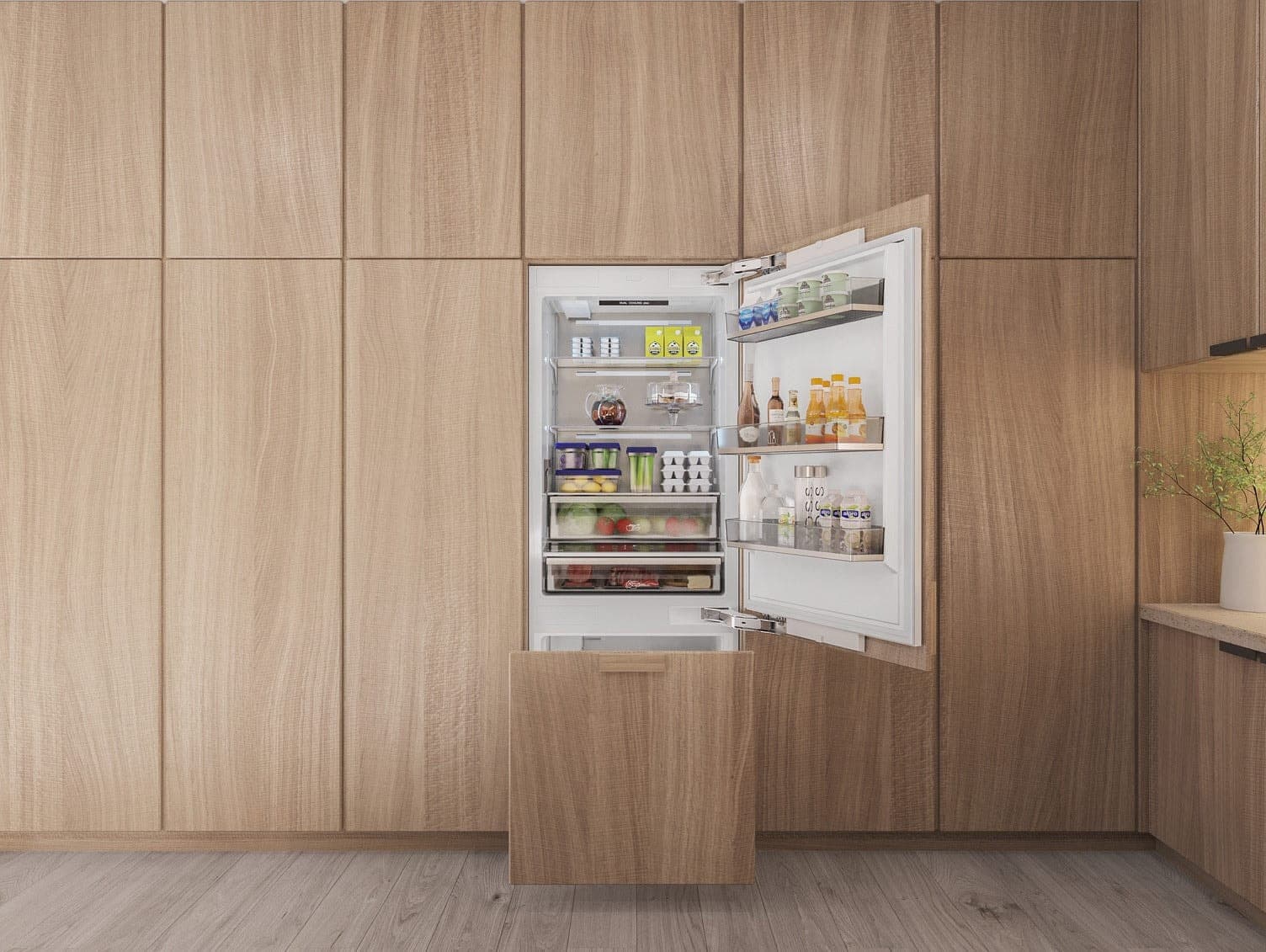 Refrigerador empotrable con la puerta abierta, con repisas y puerta llenas de alimentos y bebidas, integrado en un muro de gabinetes de madera clara de piso a techo; abajo, el cajón congelador, recubierto con el mismo panel de madera, entreabierto.