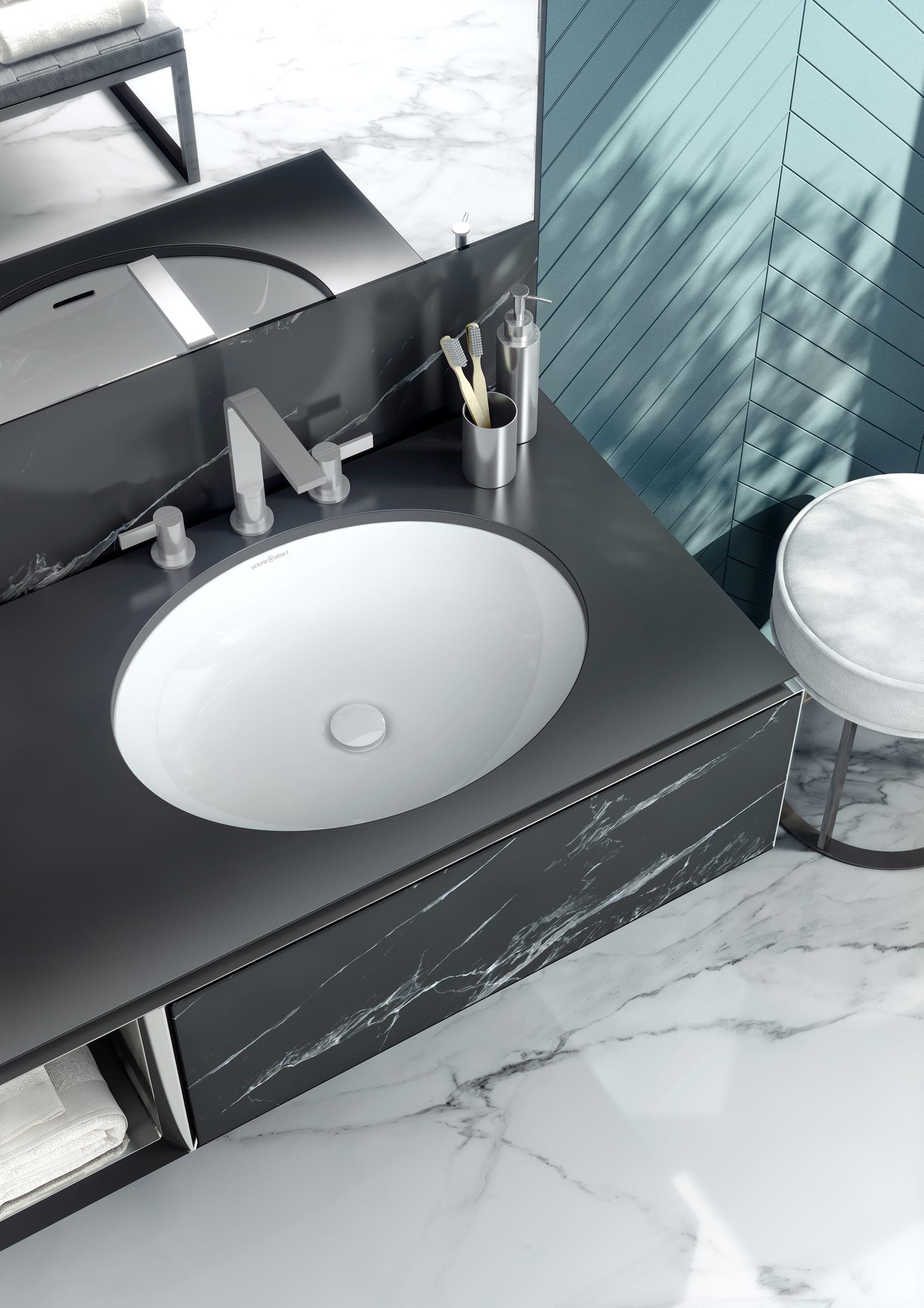 Lavabo ovalado blanco bajo una cubierta gris oscuro, con mezclador de tres piezas y un vaso con cepillos de dientes; al lado, un banco tapizado y un muro de azulejo verde azulado