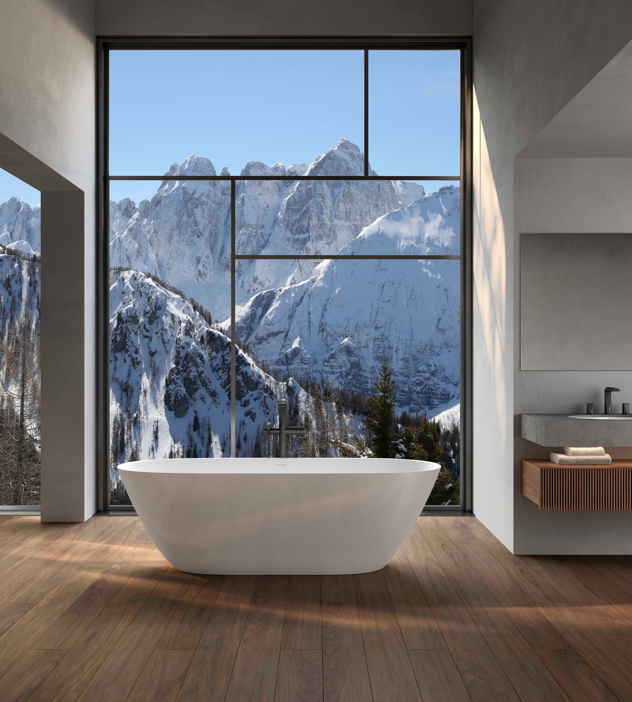 Tina exenta blanca sobre piso de madera, frente a un ventanal con montañas nevadas; a la derecha, un lavabo en una cubierta gris