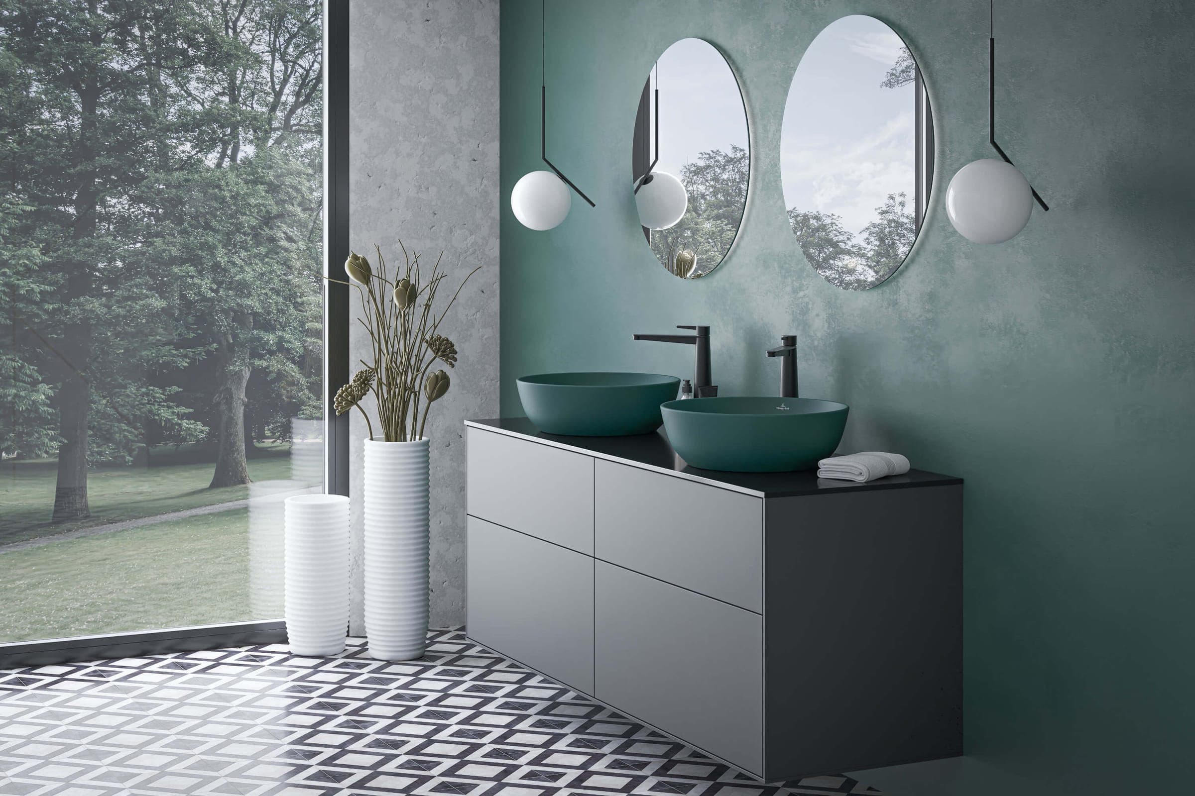 Dos lavabos sobre cubierta color azul verdoso sobre un mueble gris con cubierta negra, con grifería negra, dos espejos ovalados, lámparas esféricas y un ventanal con vista a árboles.