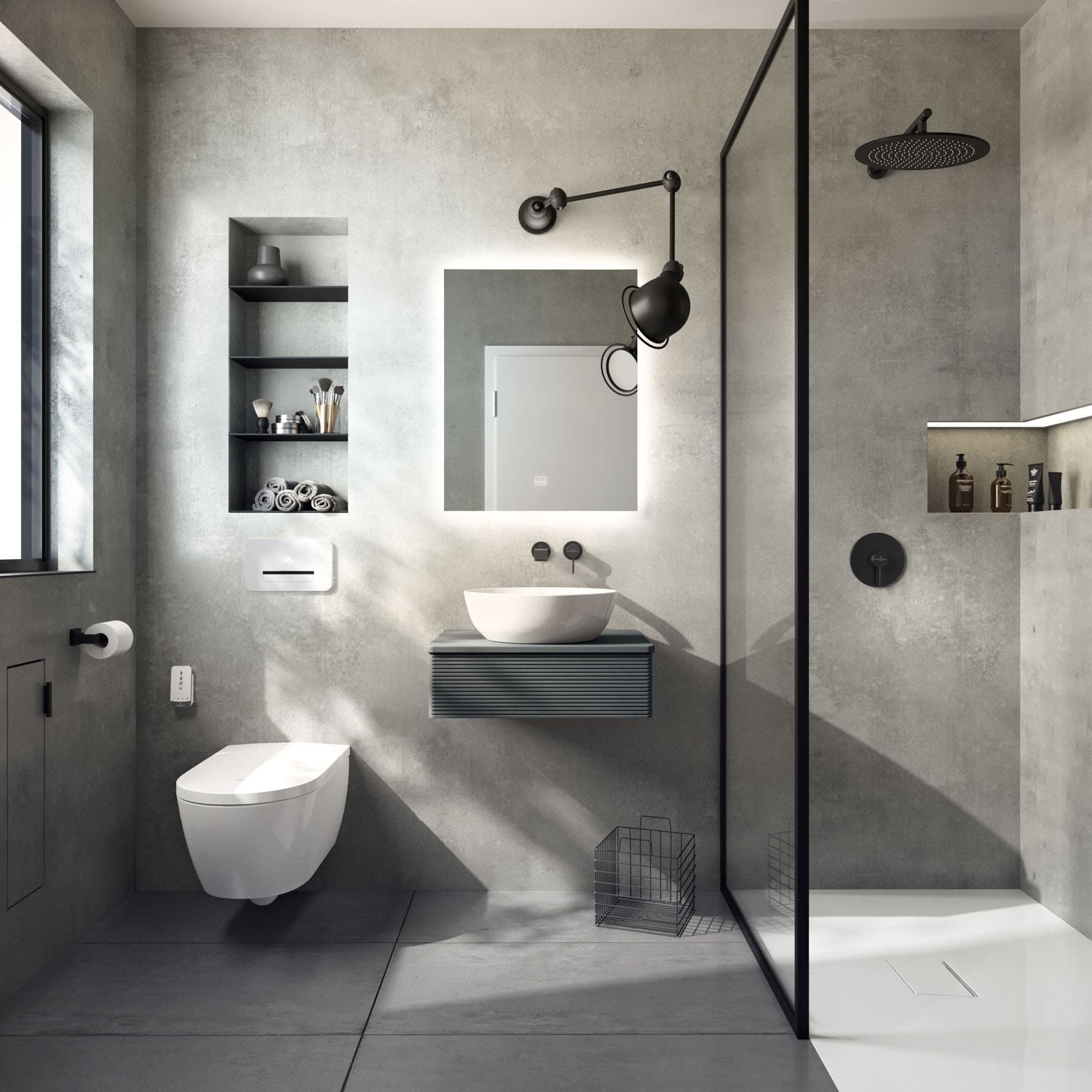 Baño de muros grises con una regadera redonda negra en brazo de pared y un control redondo negro empotrado tras un cancel de vidrio de perfil negro; a la izquierda, inodoro suspendido, lavabo sobre mueble suspendido y espejo iluminado.