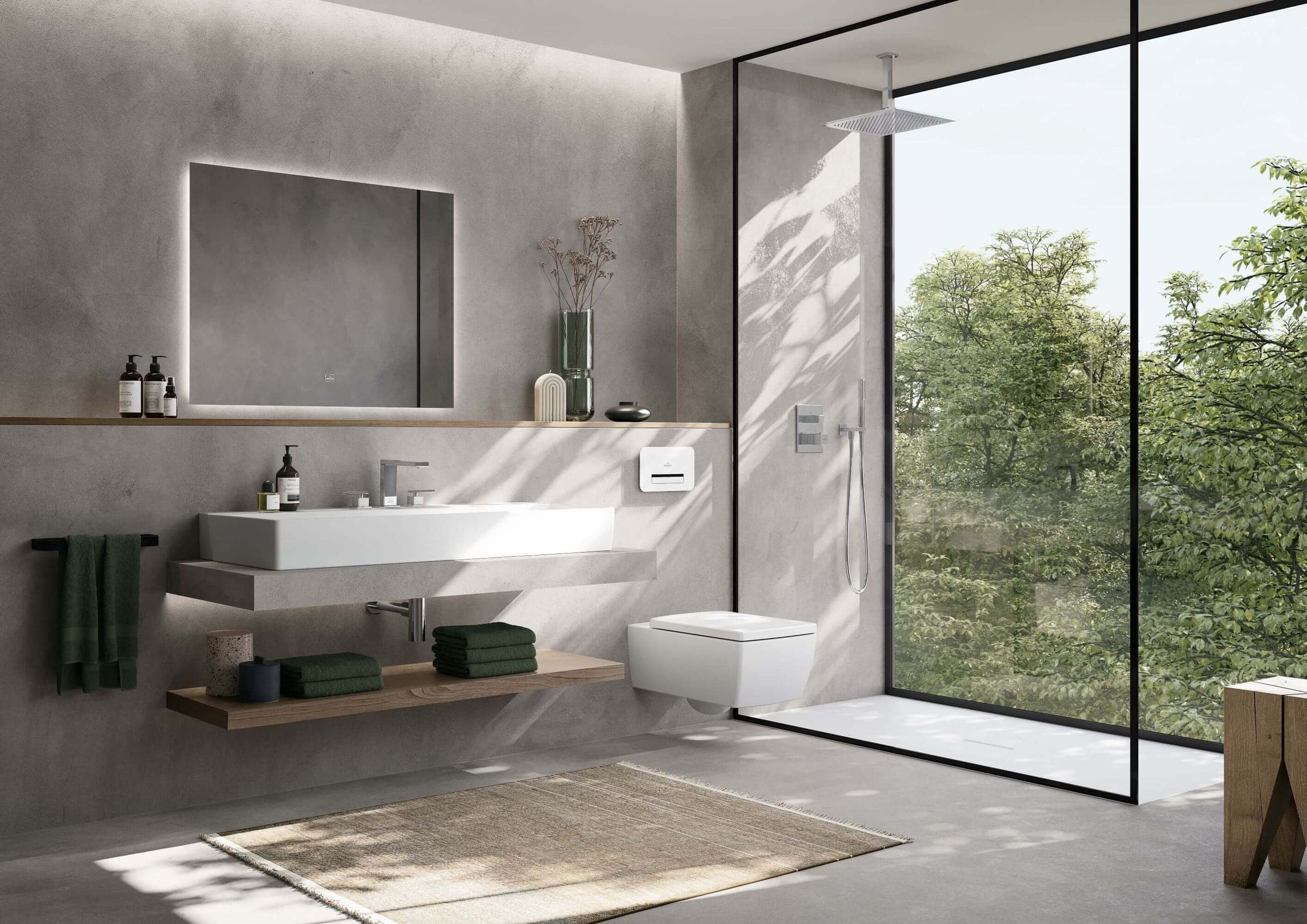 Baño minimalista de muros grises: lavabo rectangular blanco sobre repisa suspendida, inodoro suspendido de líneas rectas, espejo iluminado y regadera de techo tras un cancel de vidrio, frente a un ventanal con árboles.
