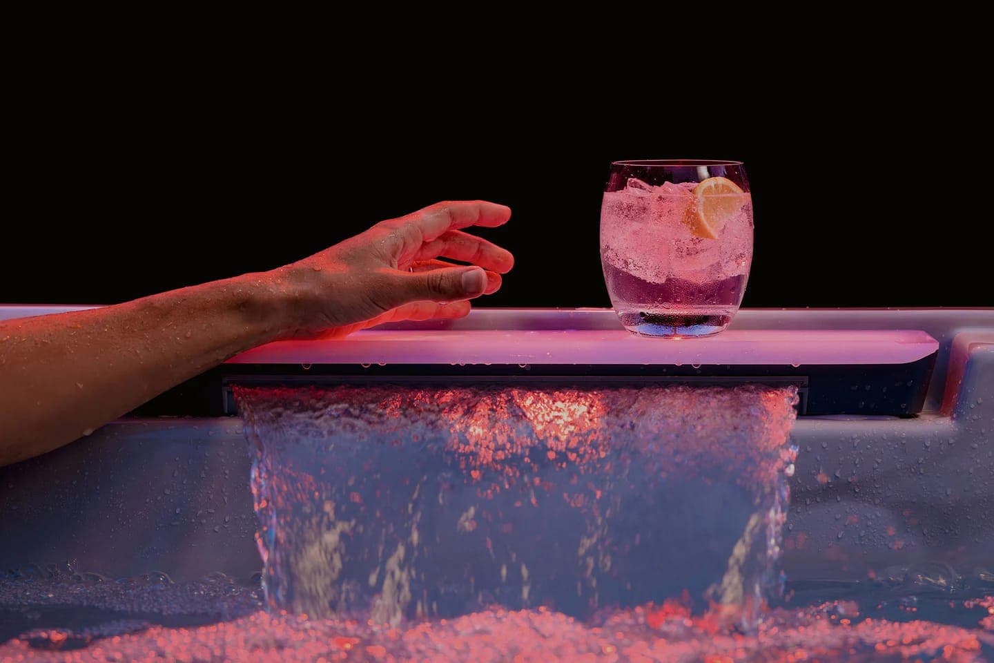 Brazo sobre el borde de un spa con una cascada y un vaso