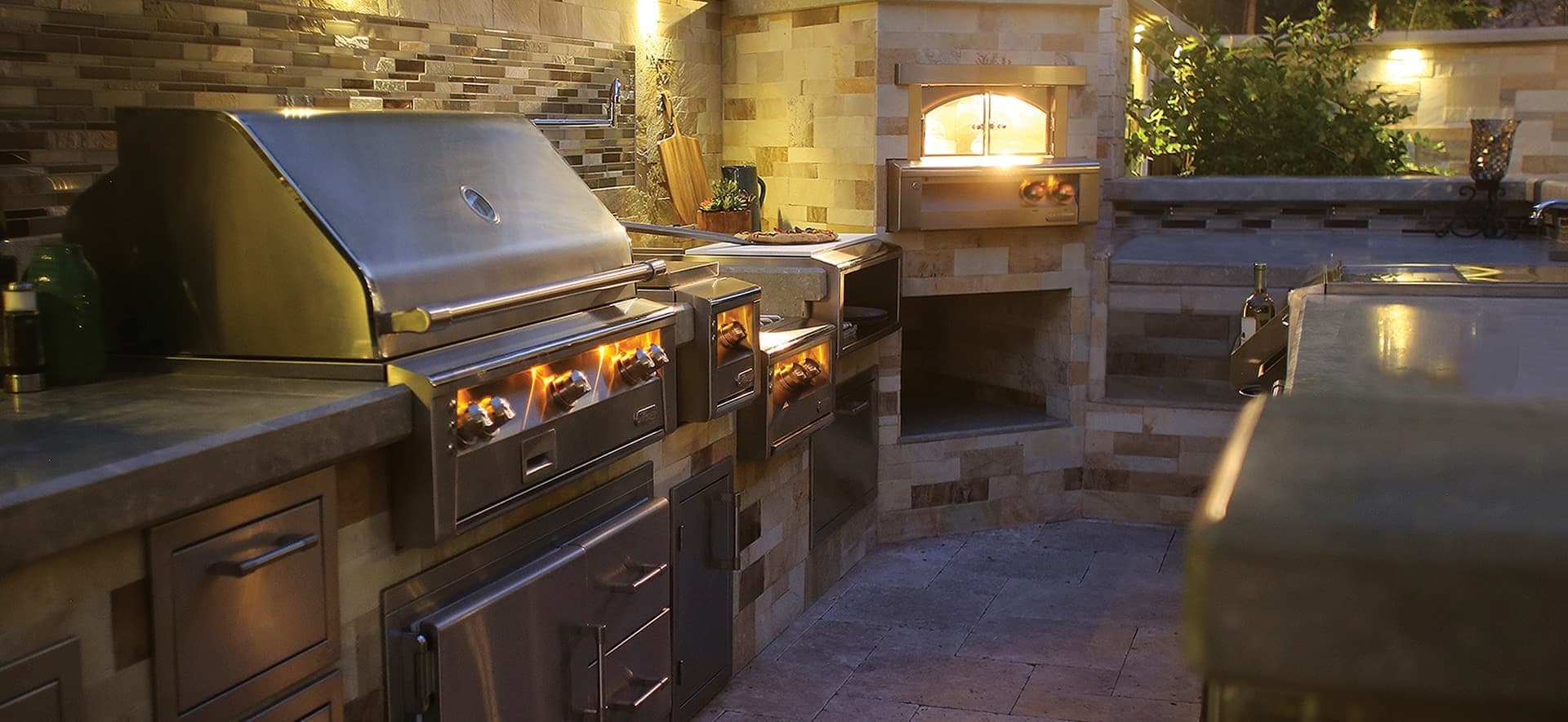 Cocina exterior de acero inoxidable con asadores y horno de leña