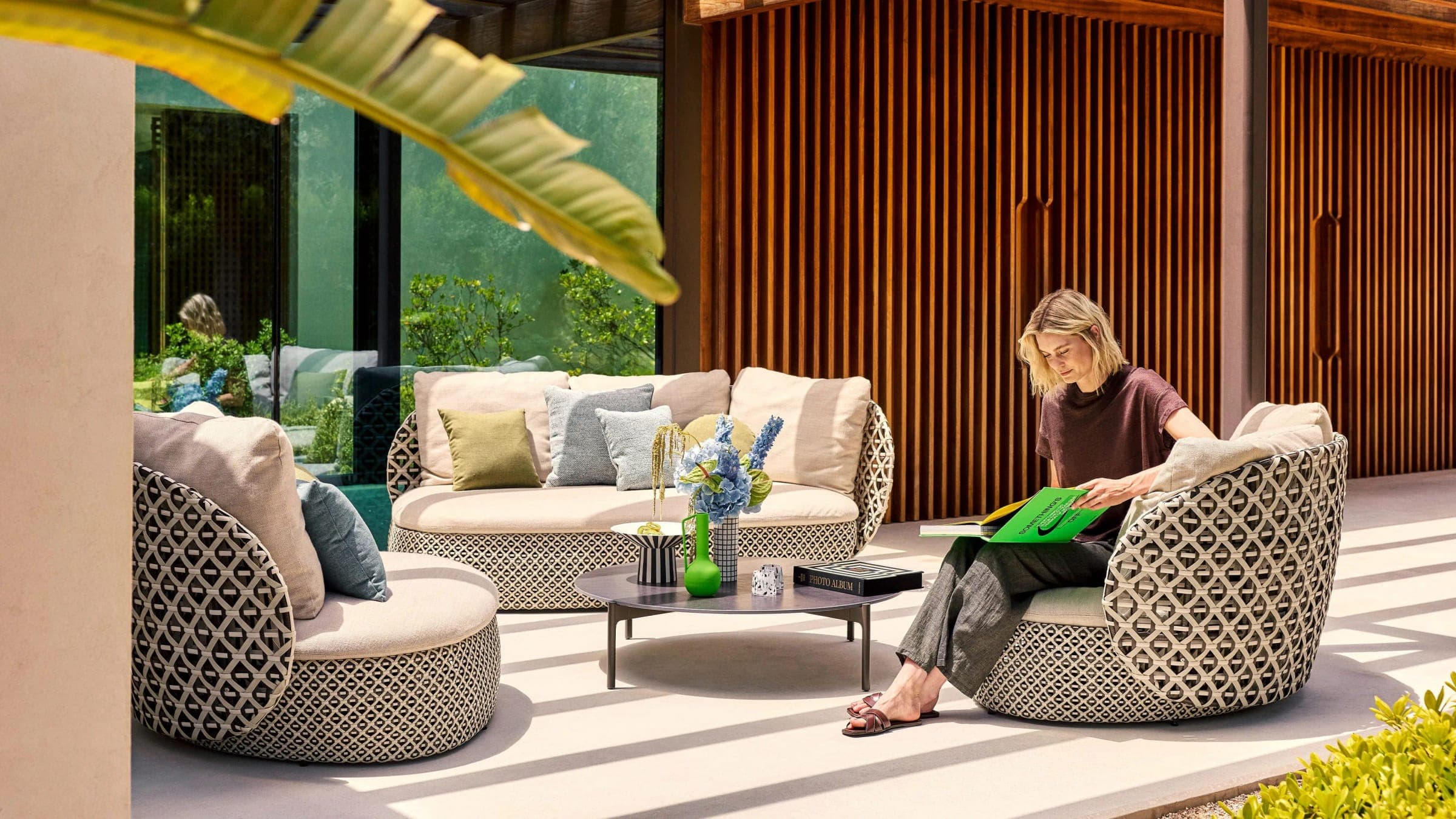Terraza con sofá y sillones tejidos, mesa de centro y una mujer leyendo