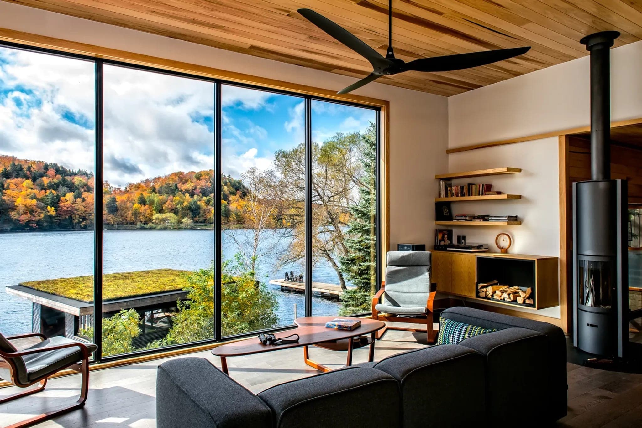 Estancia con ventilador de techo y ventanales hacia un lago