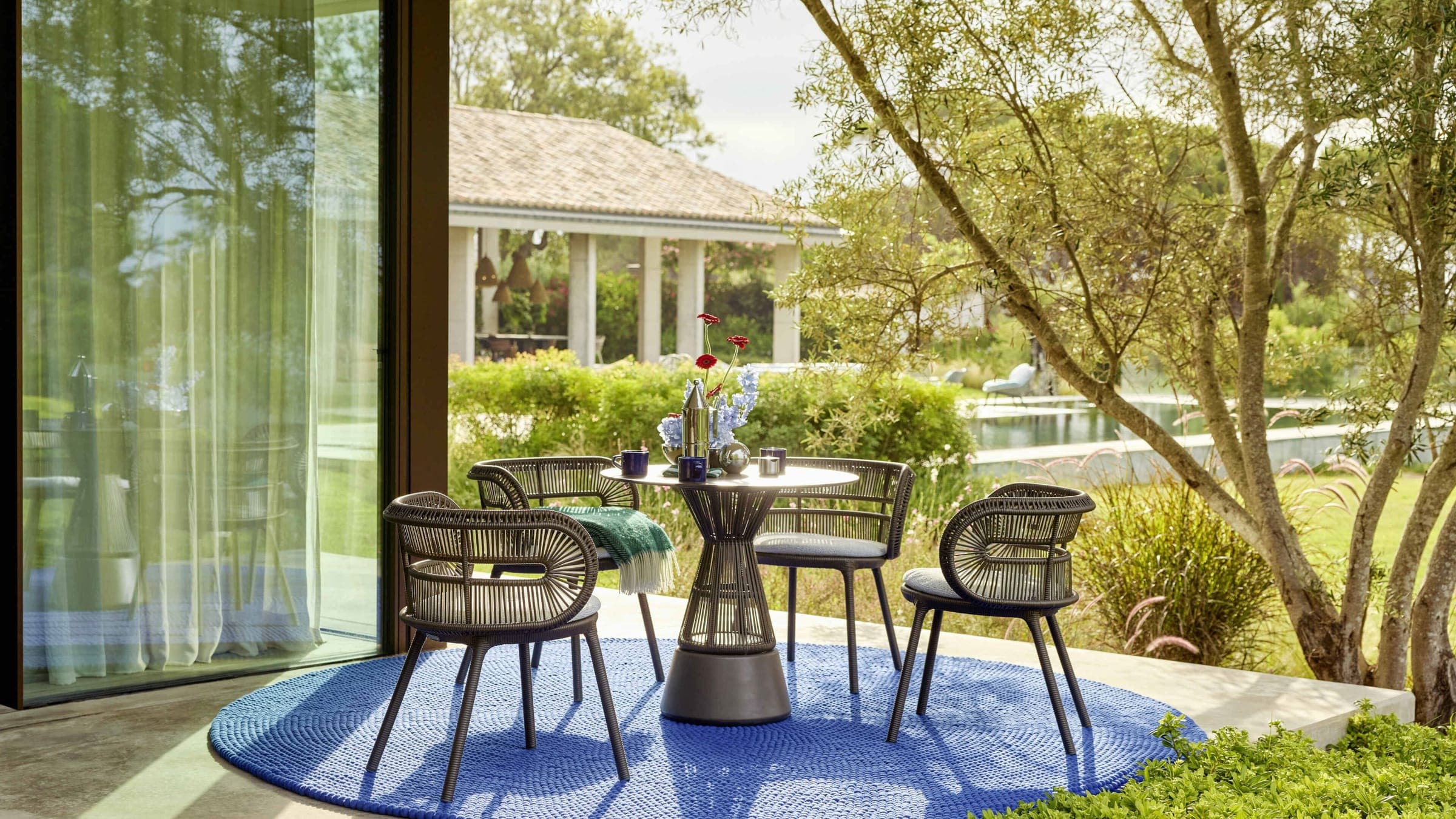 Sillas CIRQL NU alrededor de una mesa sobre un tapete azul en una terraza
