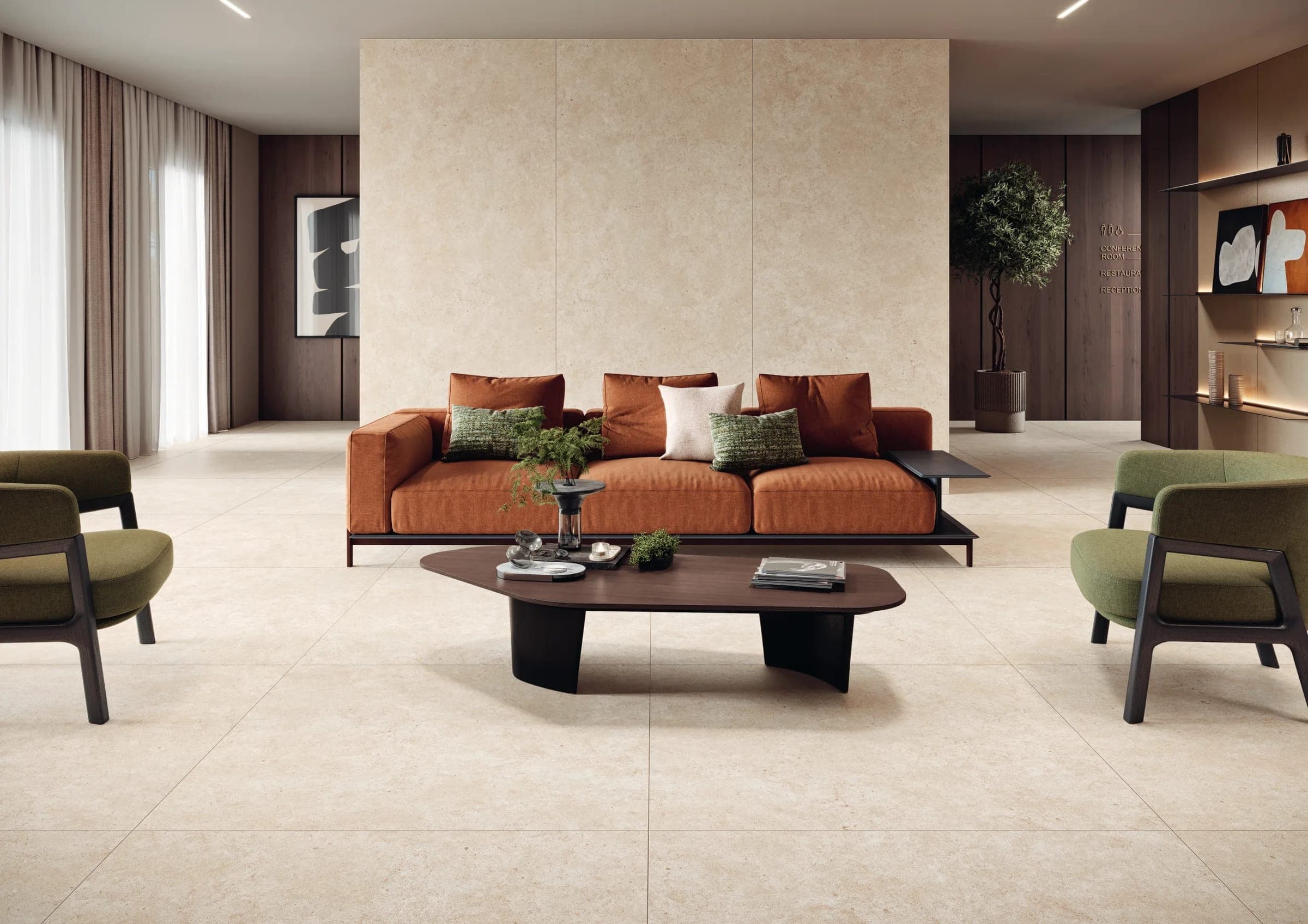 Estancia con sofá color terracota, sillones verdes y mesa de centro oscura frente a un muro exento revestido con tres placas verticales color crema con aspecto de piedra caliza; el piso es de piezas grandes del mismo tono.
