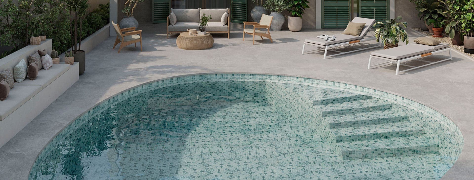 Alberca de bordes curvos revestida de mosaico en tonos verde agua, con escalones bajo el agua, junto a una terraza gris con un sofá, sillones, una mesa baja tejida, camastros y plantas en macetas.