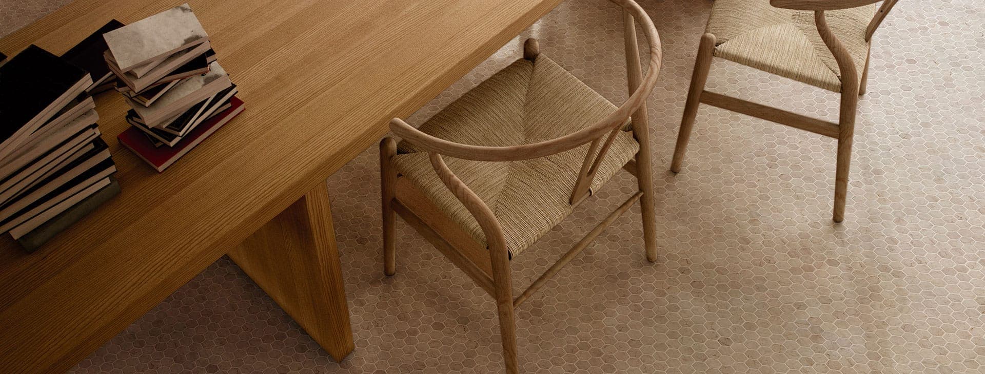 Vista desde arriba de una mesa de madera y dos sillas de madera con asiento tejido sobre un piso de mosaico hexagonal en tono beige.