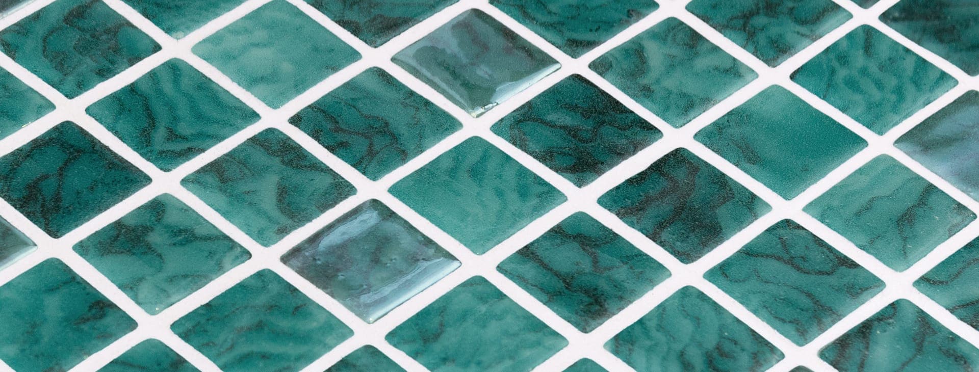 Acercamiento en diagonal a teselas cuadradas de vidrio verde esmeralda con vetas oscuras onduladas, separadas por juntas blancas; algunas brillan con reflejos claros.