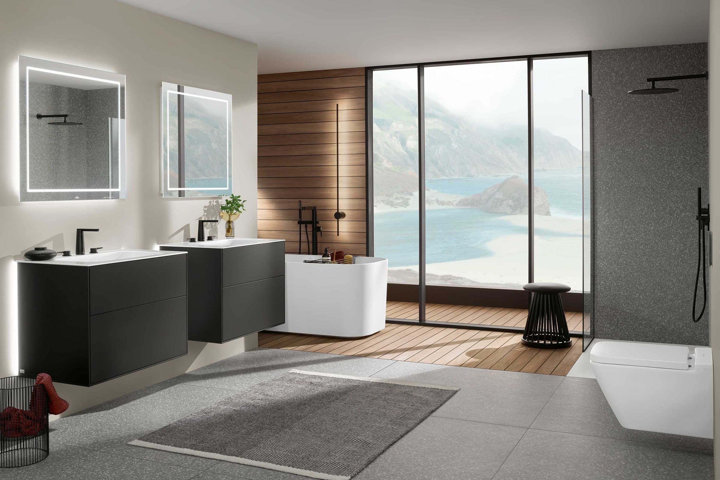 Baño con dos muebles de lavabo negros, espejos iluminados, tina exenta y vista al mar